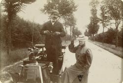 Arrêtés sur une route déserte et bordée d’arbres, le conducteur et sa passagère dans une Renault de type D 1901